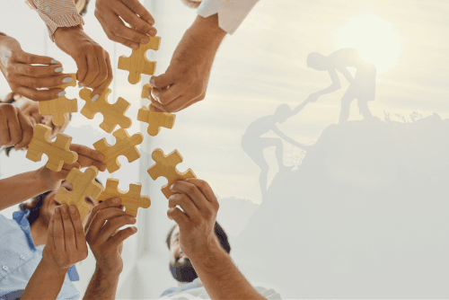 Plusieurs mains de personnes diverses tenant des pièces de puzzle dorées, symbolisant le travail d’équipe ou la collaboration